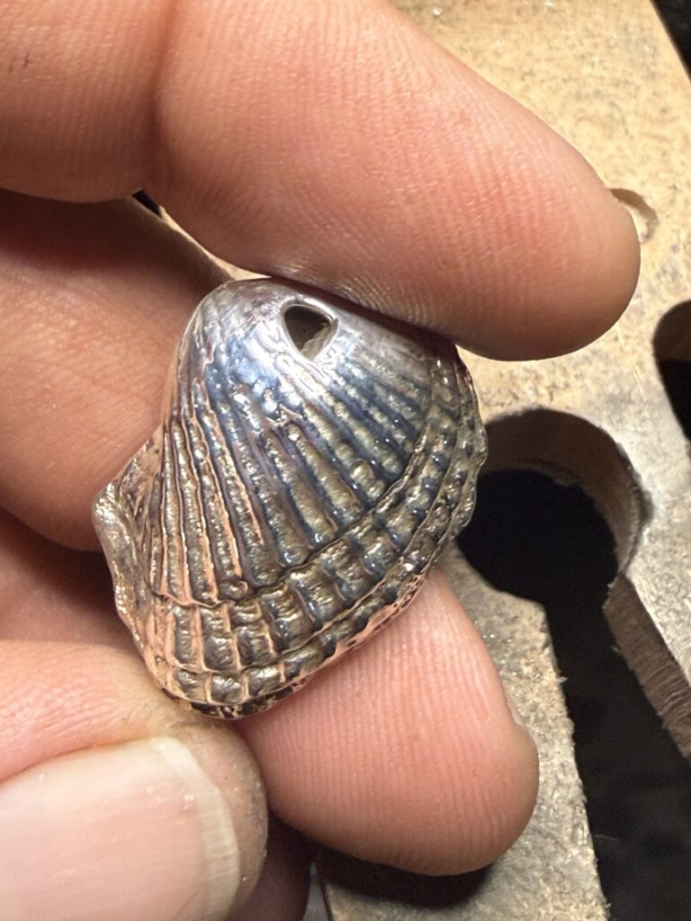Handgemaakte schelp hanger met geribbeld reliëf in de hand van de maker